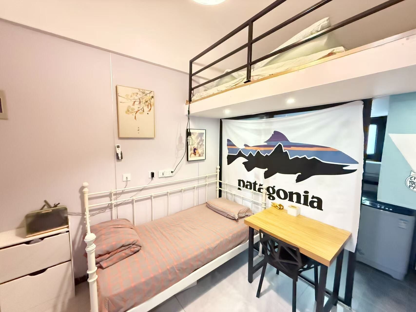 A bunk bed room with a desk, a bed with a patterned blanket, a wall-mounted artwork, and a large poster of a mountain range.