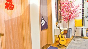 Una habitación con una puerta de madera, un árbol de flores rosadas, una guitarra, un tambor y una silla amarilla.