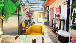Un estrecho callejón con un sofá amarillo, una mesa con una taza y una botella, y una cortina verde.