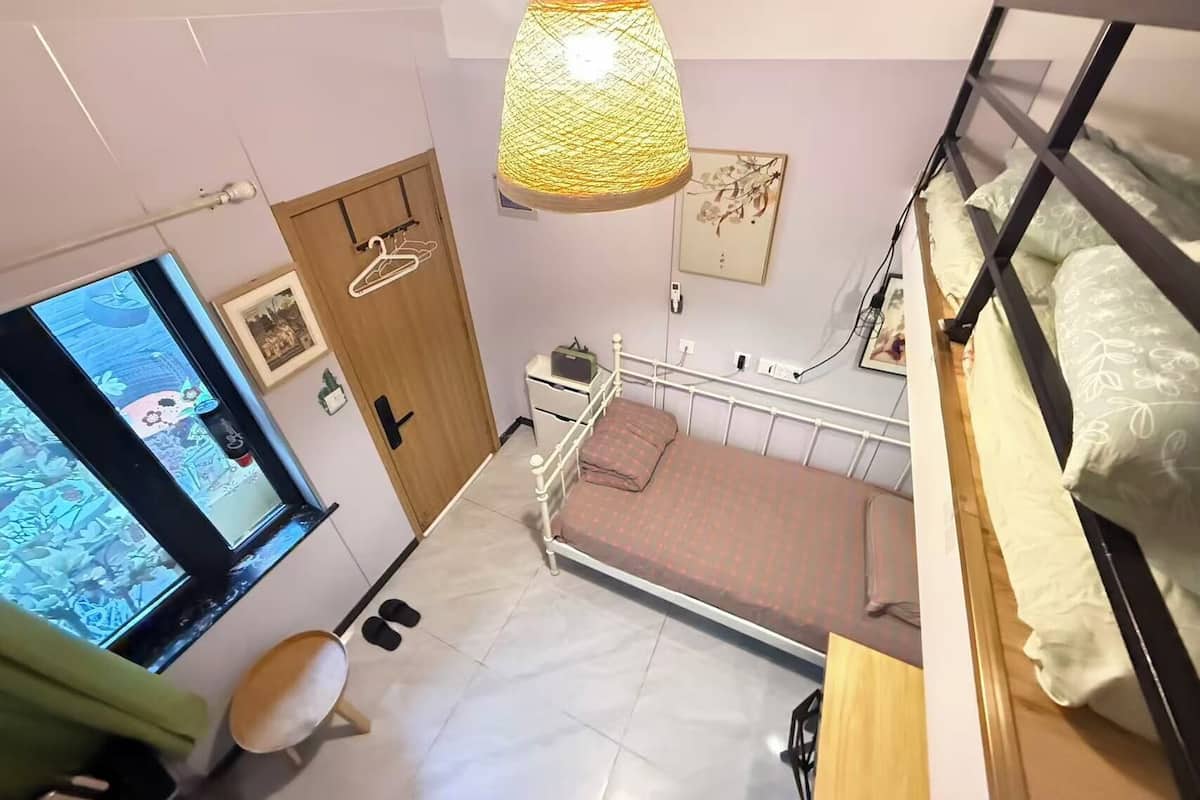 A bedroom with a bunk bed, a hanging lamp, a TV, and a door with a hanger.