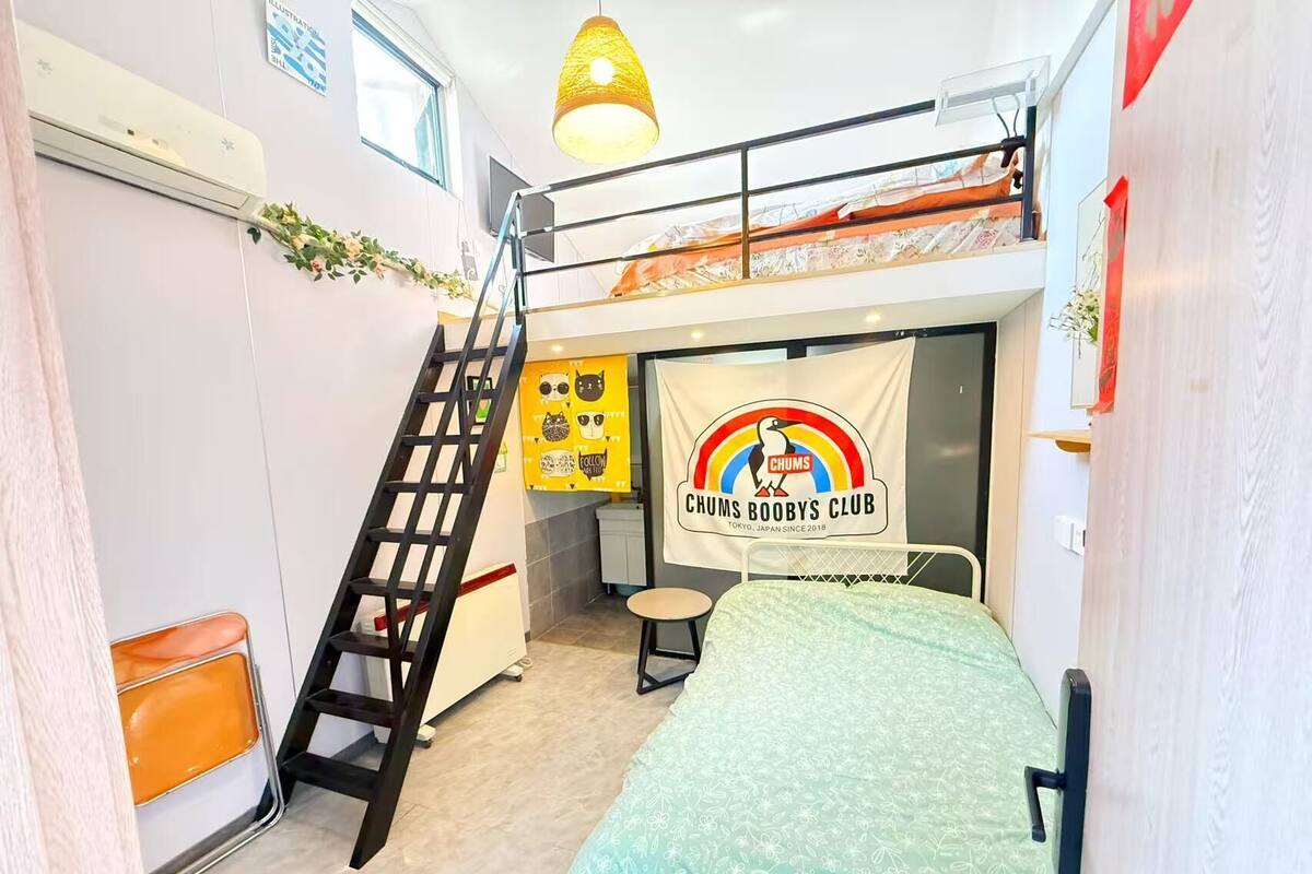 A bunk bed room with a ladder, a small table, a chair, and a banner for Chums Boobys Club.