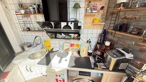 Cocina compacta con lavavajillas, microondas y pileta. Se observan estantes con diversos utensilios de cocina y un reloj en la pared.