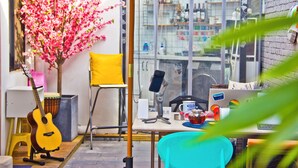 Una habitación con escritorio, silla, guitarra, planta y ventana con vista a la calle.