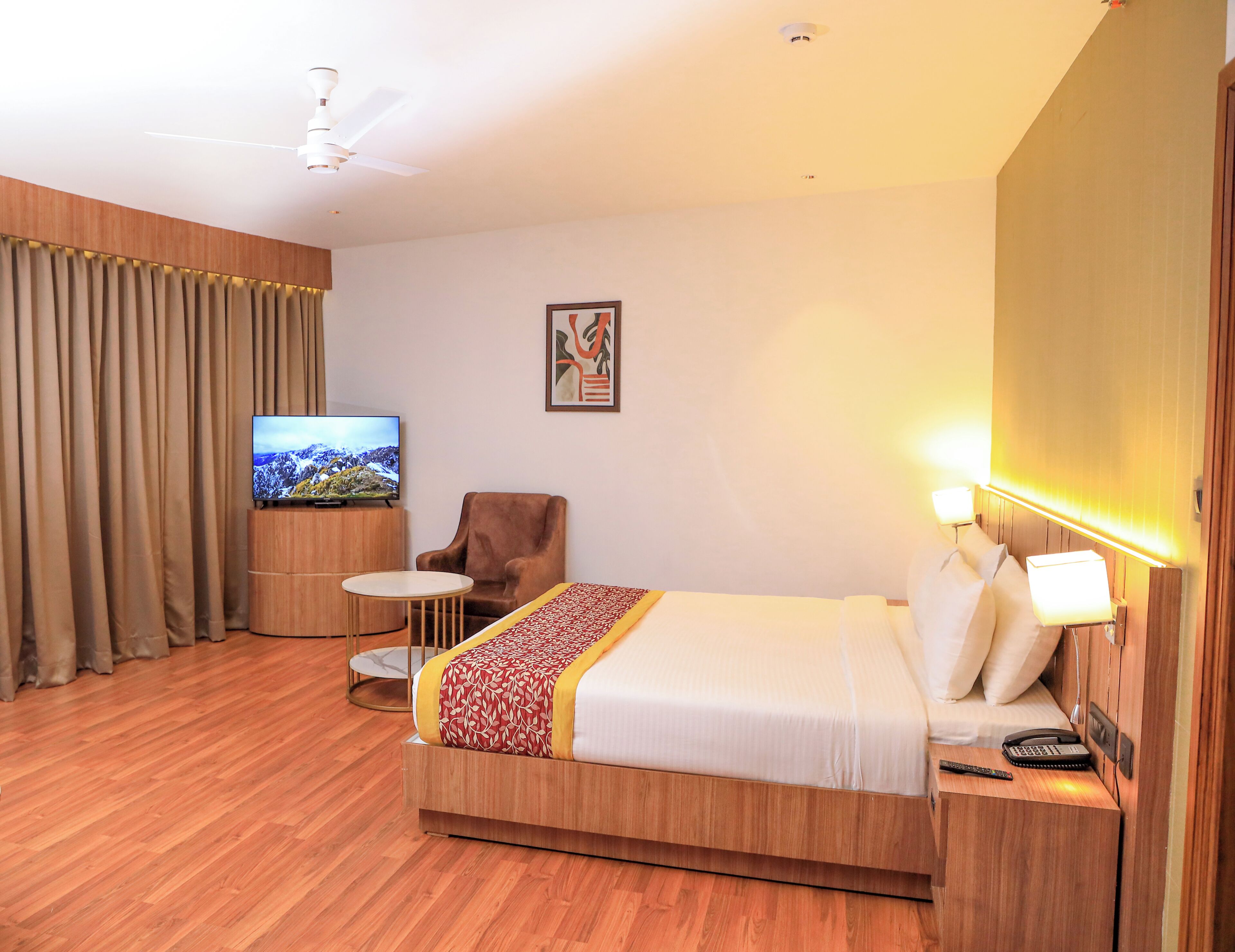A hotel room with a bed, a TV, a chair, a small table, and a bedside lamp.