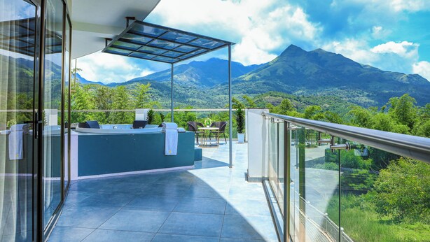 Un balcón con barandilla de vidrio, una zona de estar con mesa y sillas, y vistas a las montañas.