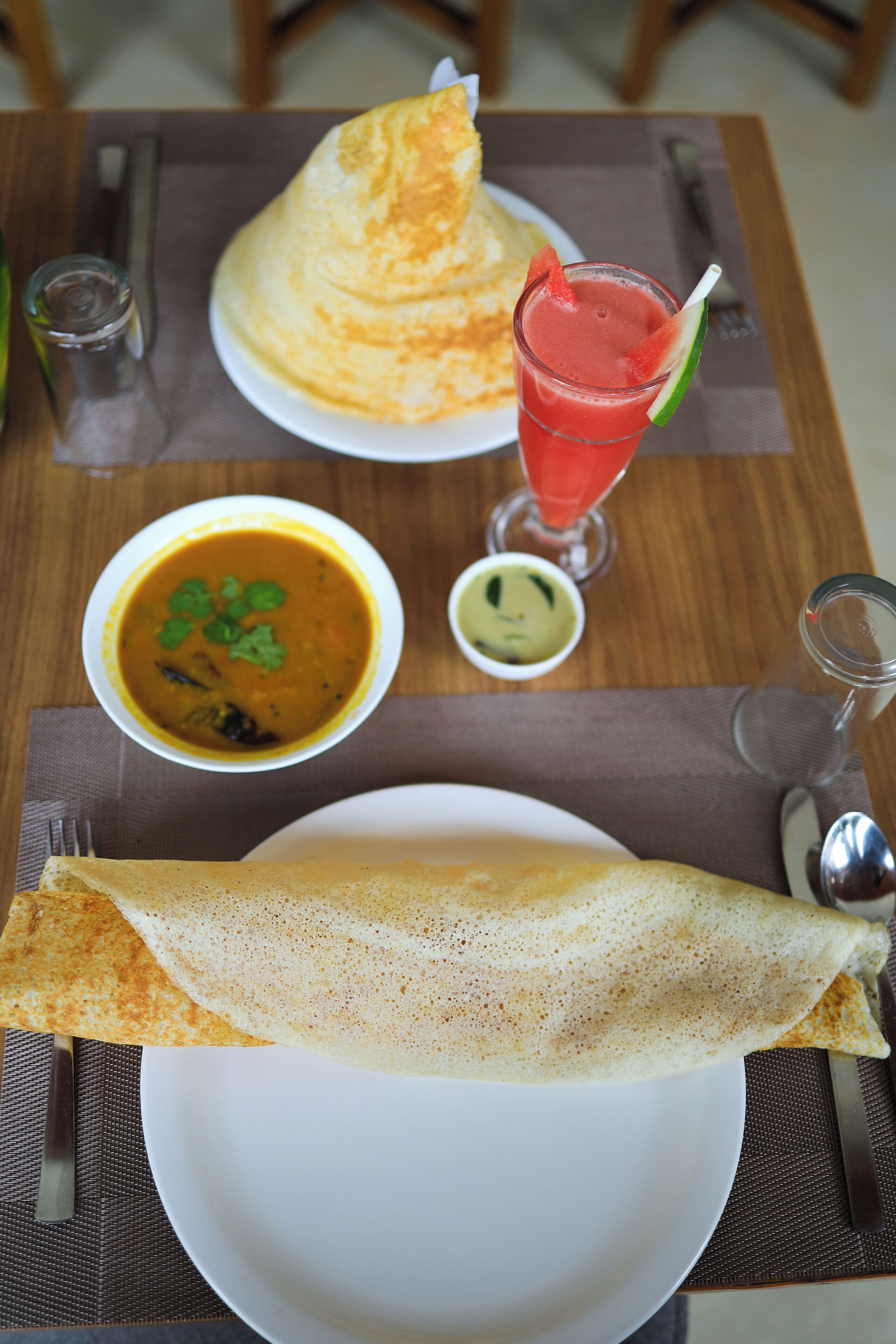 En tallerken med en foldet crepe, en skål suppe og et glas rød drik på et bord.
