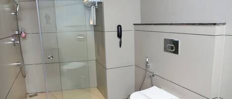 A modern bathroom with a glass shower enclosure, a white toilet, a trash bin, and a telephone mounted on the wall.
