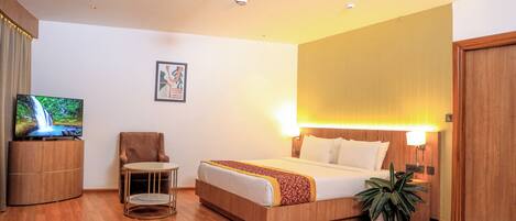 Habitación de hotel con cama, televisión, una silla, ventilador de techo y lámpara de pared.