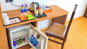 Habitación compacta con escritorio de madera, una silla, refrigerador, cafetera y un cuadro colgado en la pared.