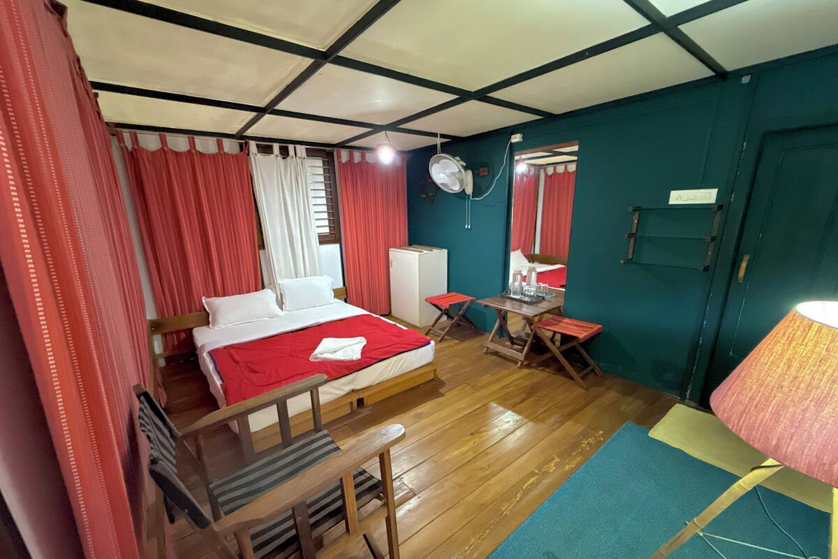 Una habitación con cama, escritorio, silla, ventilador y lámpara.