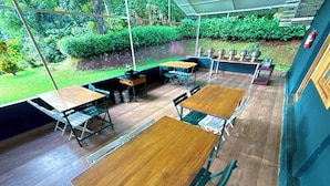An outdoor dining area with wooden tables and chairs, surrounded by greenery and a covered section. - Whispering Willows (Mudumalai)