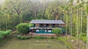 A two-story building with a balcony, surrounded by dense forest and a pond.