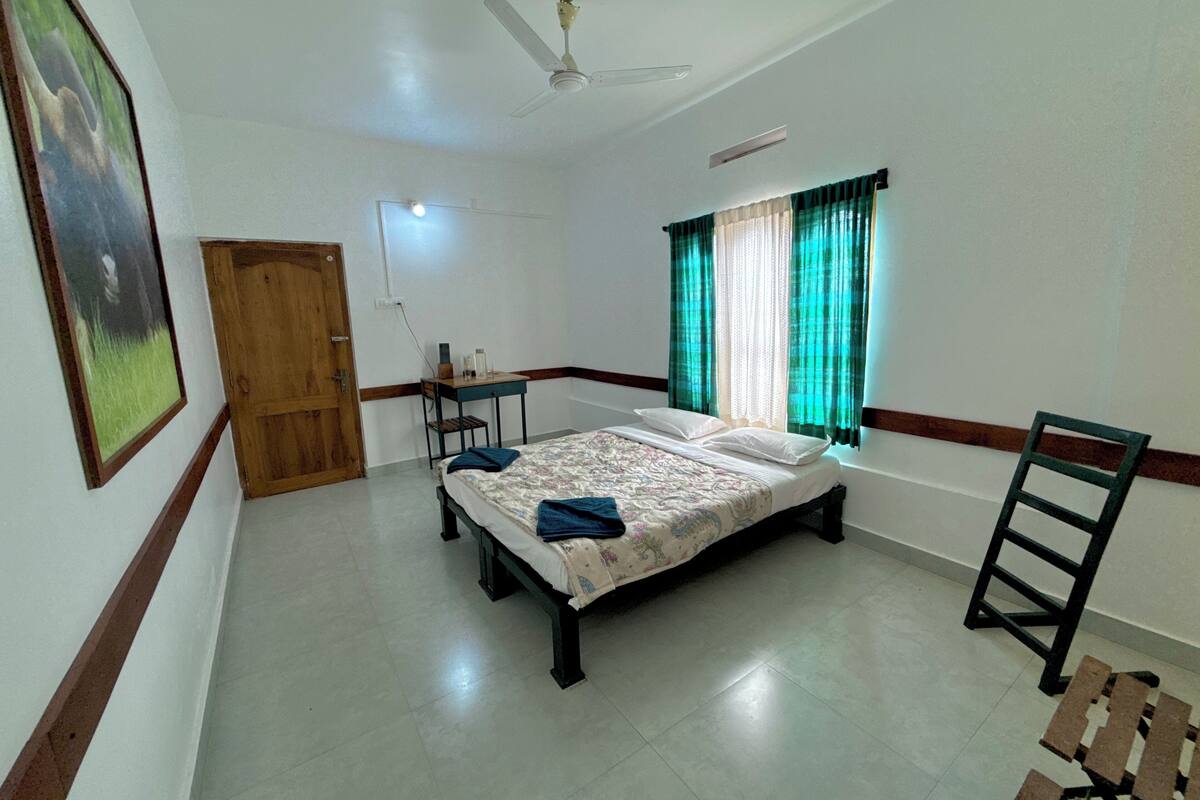 Una habitación con cama, escritorio, silla, ventilador de techo y ventana con cortinas.