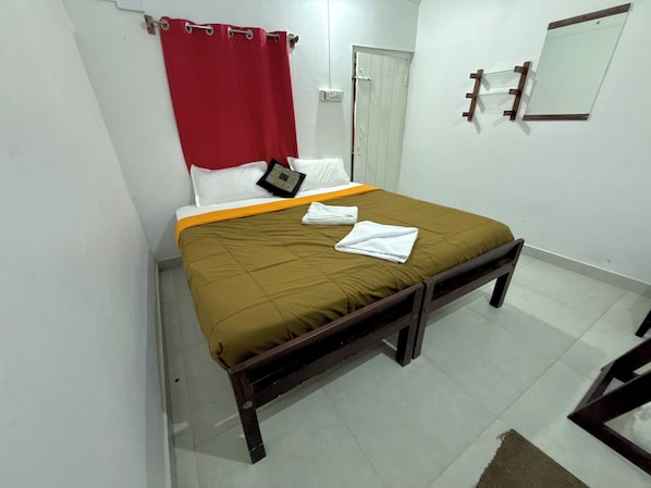 Una cama individual con una colcha marrón, almohadas blancas y una cortina roja.