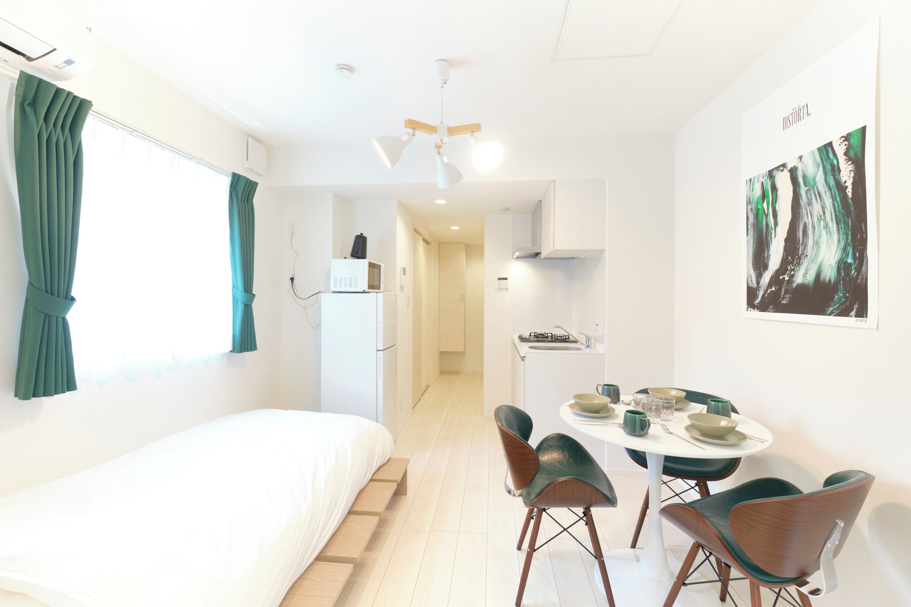 A modern room with a bed, a dining table with chairs, a kitchen area, and a ceiling fan.