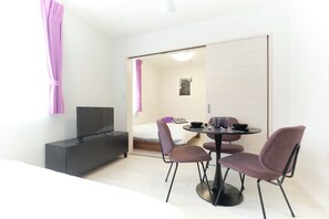 Quarto moderno com cama, televisão, mesa de jantar com cadeiras e um pequeno armário.