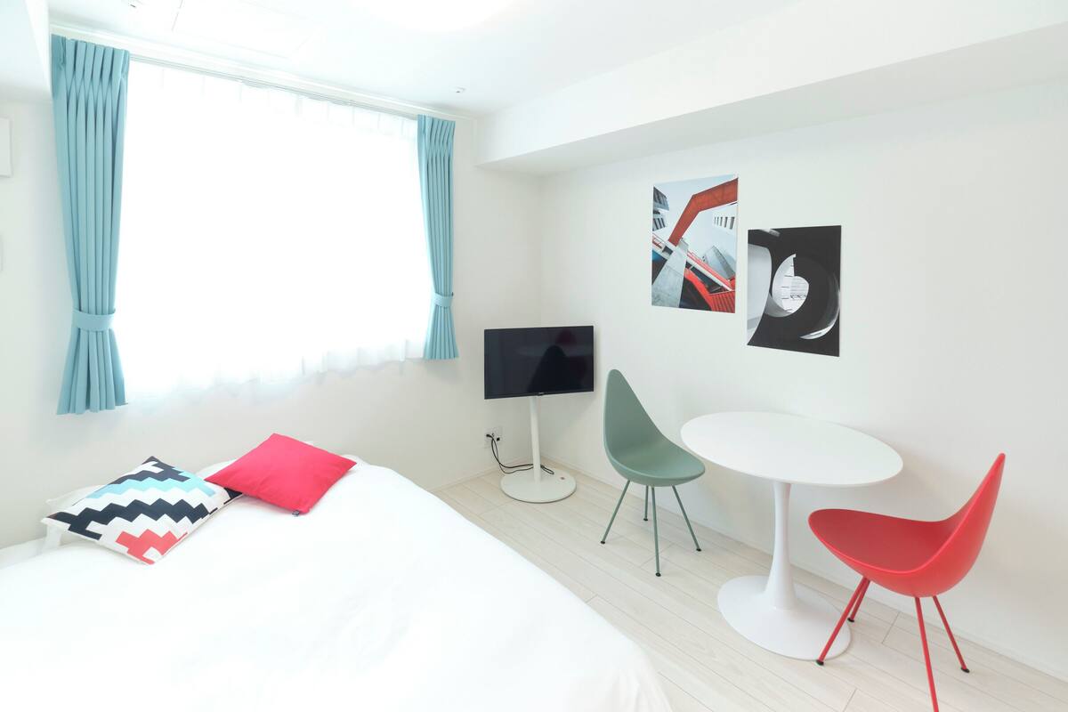 A modern hotel room with a bed, a TV, a small table, two chairs, and artwork on the wall.