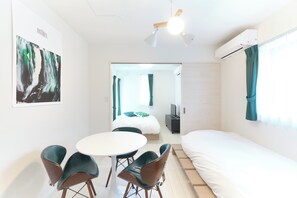 A modern hotel room with a bed, a dining table with chairs, a ceiling fan, and a painting on the wall. - Sugamo Green Heights by Tranova 2 (Tokyo)