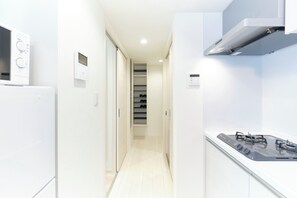 Um corredor estreito com um refrigerador branco, forno embutido, fogão a gás e termostato fixado na parede.