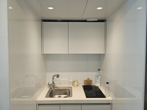 A modern bathroom with a stainless steel sink, a black electric stove, and a cabinet above the sink. - RedRoof (Seoul)
