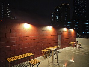 Una terraza en la azotea con paredes de ladrillo, mesas y sillas de madera, e iluminación con luces empotradas.