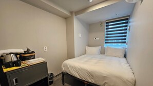 Um quarto pequeno e bem organizado, com uma cama, mesa de cabeceira, dispensador de água e janela com persianas.