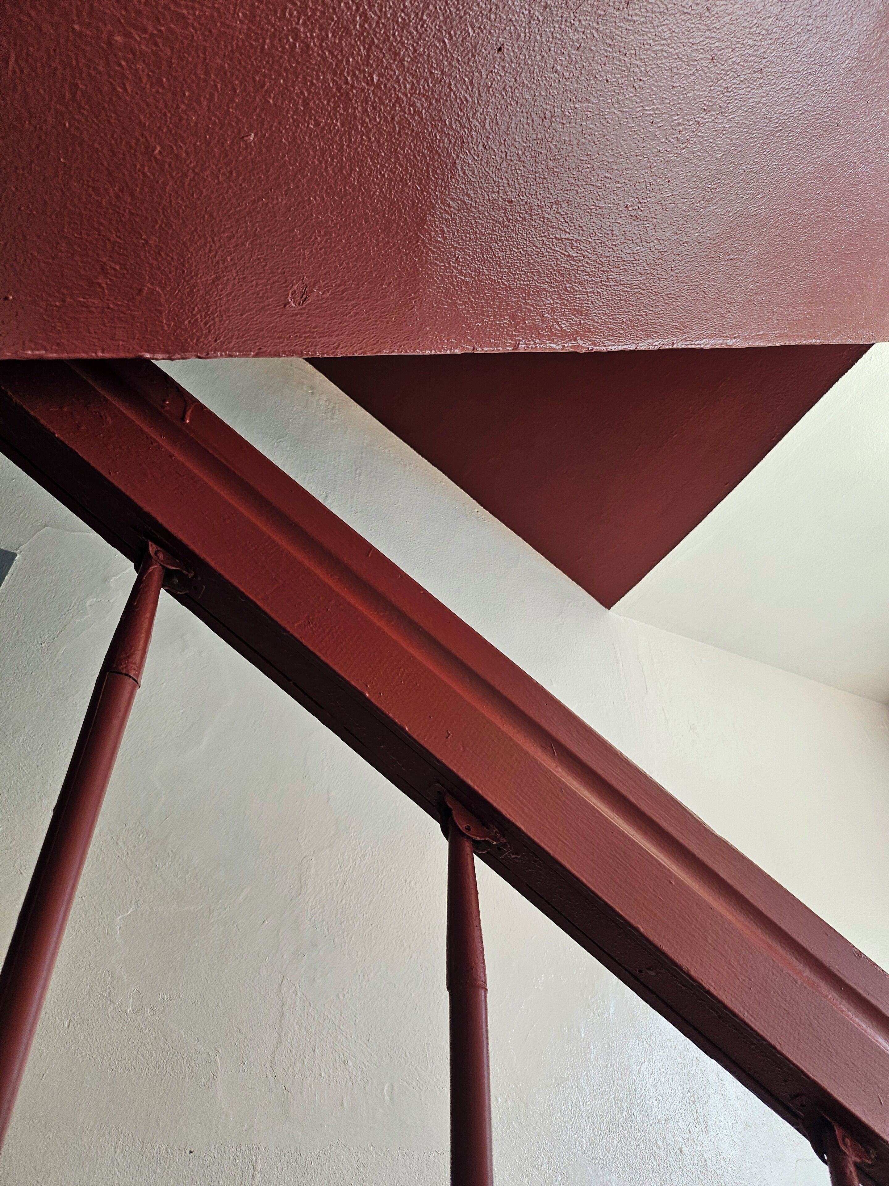 A close-up of a red metal staircase railing with a white wall in the background.