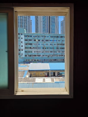 Vista a través de una ventana de un edificio de varios pisos con techo azul, rodeado de edificios más altos.