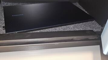 Een zwart Samsung apparaat op een gestructureerd oppervlak, een witte lade eronder en een metalen frame.