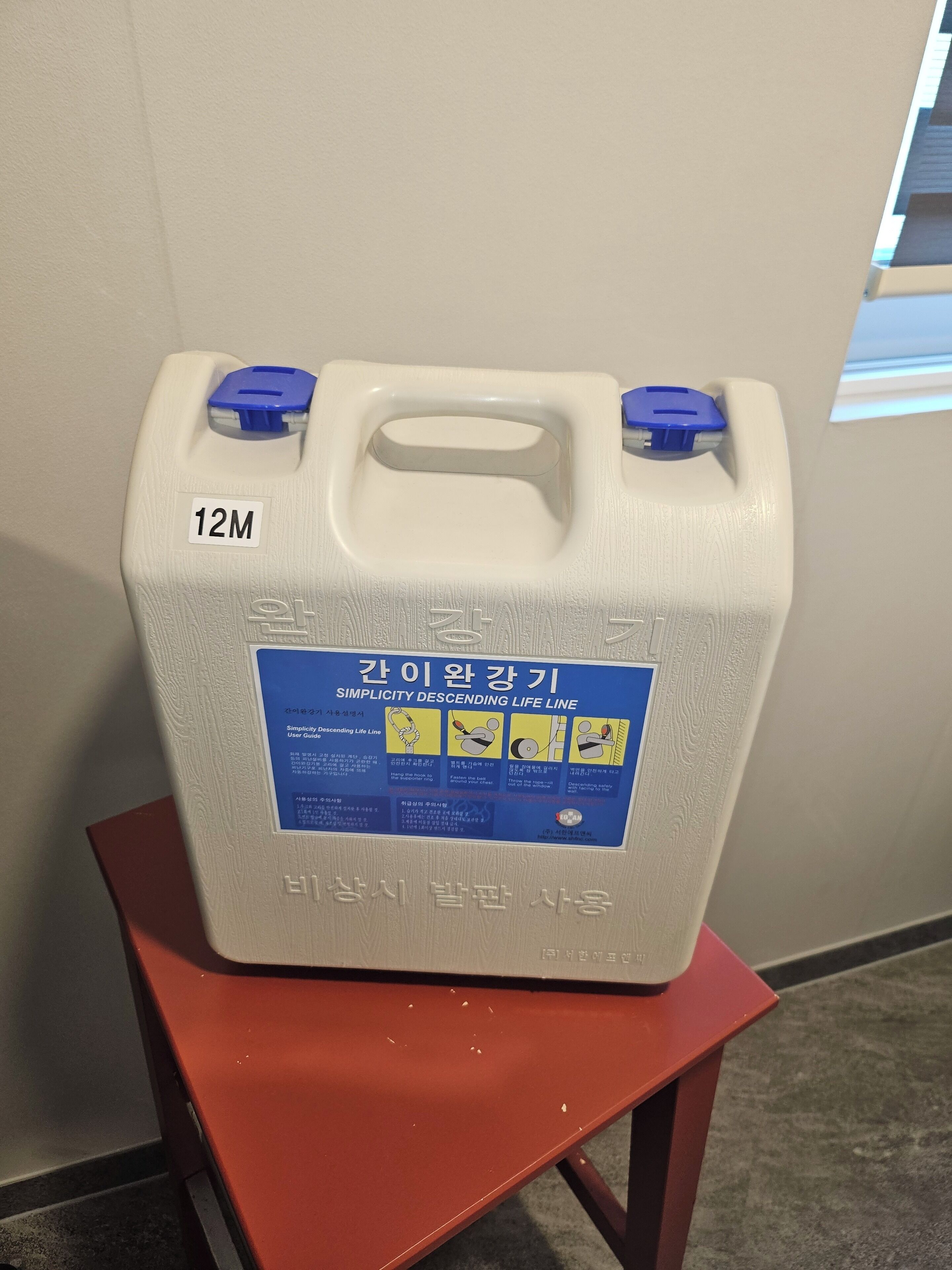 A white plastic container with a blue label on a red stool.