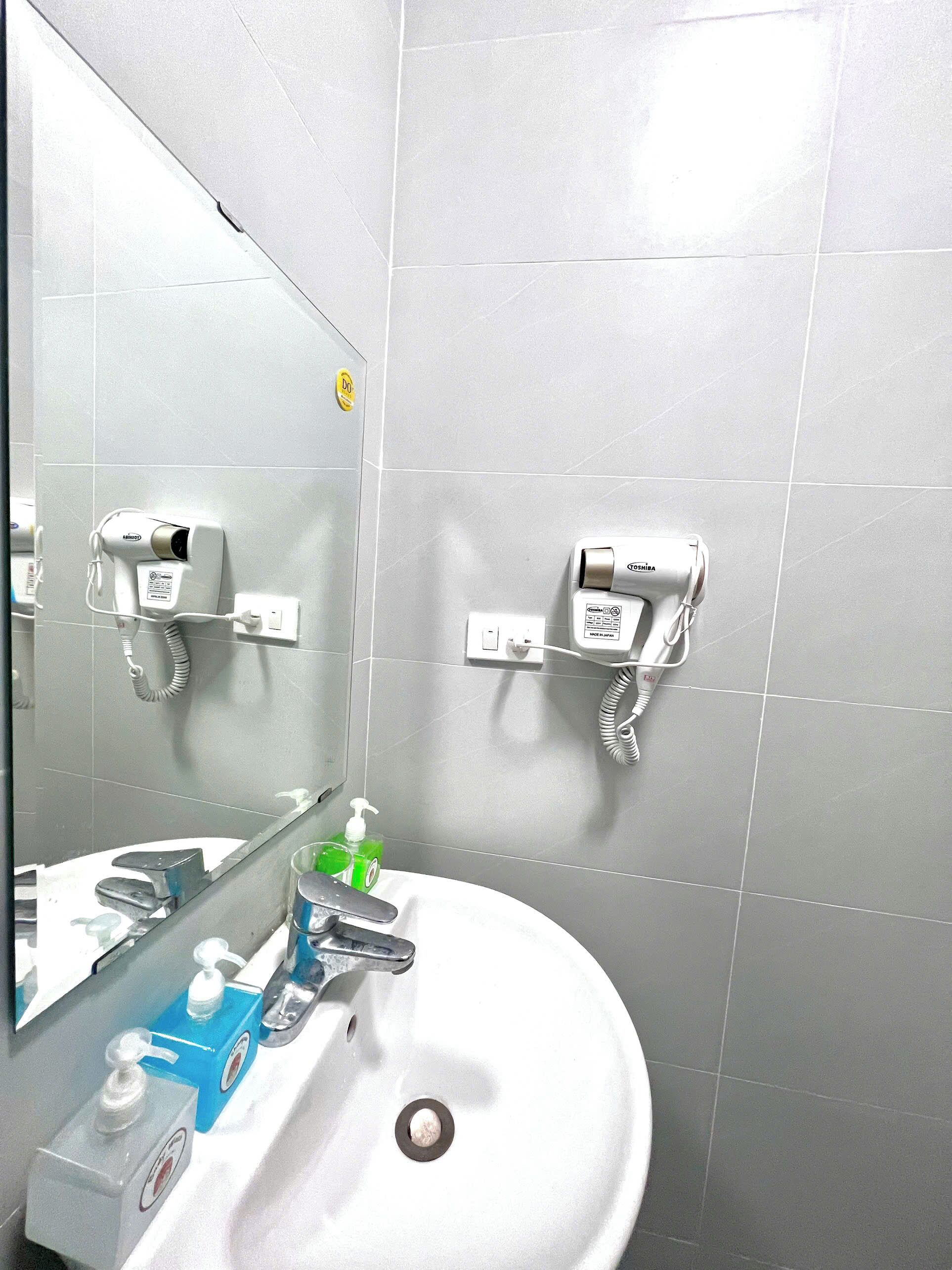 A bathroom with a sink, mirror, and two hair dryers mounted on the wall.