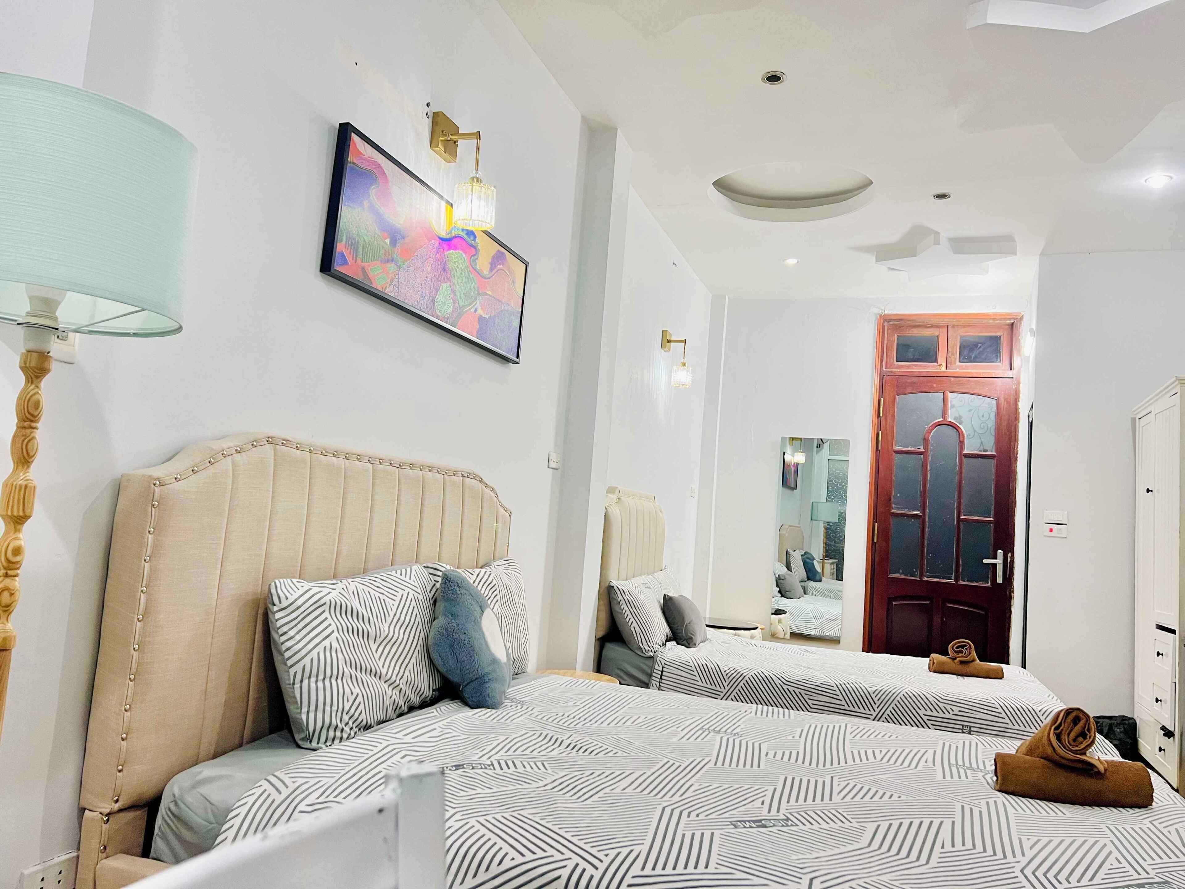 Een hotelkamer met twee bedden, een grote spiegel, een houten deur en een plafondlamp.