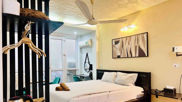 Un dormitorio con cama, ventilador de techo, proyector montado en la pared y ventana con cortinas estampadas.