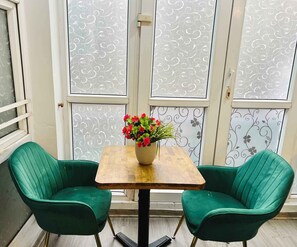 Una habitación con dos sillas verdes, una mesa de madera con un florero y un papel tapiz estampado.