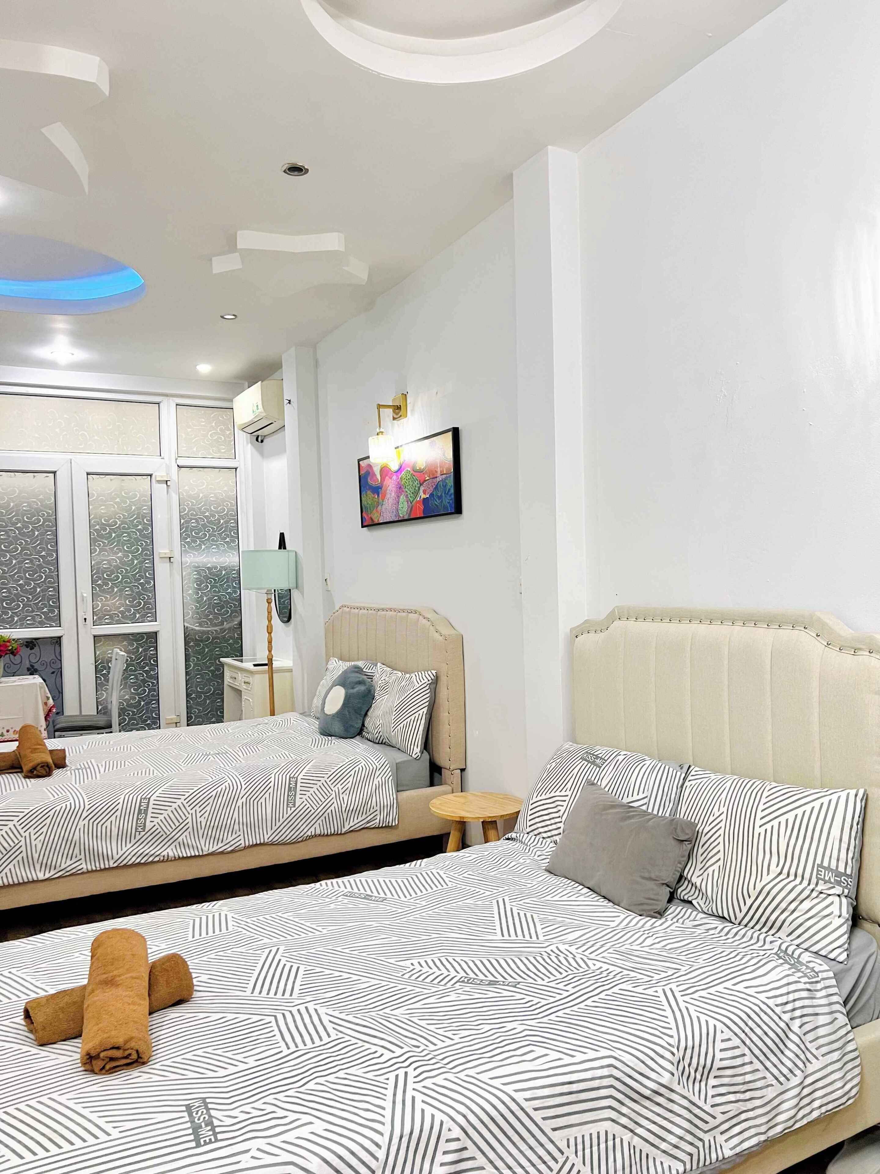 A hotel room with two beds, a large window, a painting, and a ceiling light fixture.