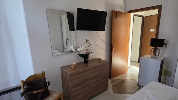 Habitació d'hotel amb un llit, un taulell de nit de fusta, una cadira, un televisor fixat a la paret i una porta que dona a una altra habitació.