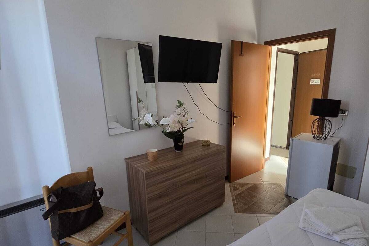 Une chambre d’hôtel comprenant un lit, une commode en bois, une chaise, un téléviseur fixé au mur et une porte donnant sur une autre pièce.