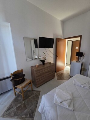 Ein Hotelzimmer mit einem Bett, einer Holzkombination, einem Sessel, einem an der Wand montierten Fernseher und einer Tür zu einem anderen Raum.