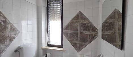 A bathroom with a toilet, bidet, sink, and a window with lace curtains.
