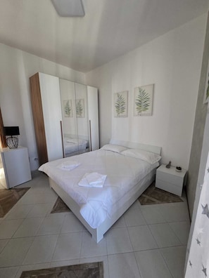 Een slaapkamer met een bed, een kledingkast, een nachtkastje en twee ingelijste botanische prints aan de muur.