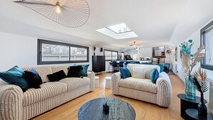 Un salon moderne avec un canapé, une table basse et, au fond, un coin repas.