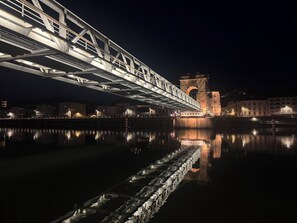 Una vista nocturna d'un pont sobre un riu tranquil amb edificis a la riba contrària.