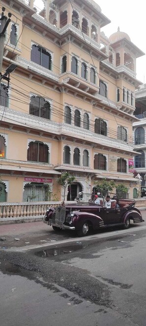 A multi-story building with ornate balconies and a vintage car parked in front. - Moti Mahal Muroli (Udaipur)