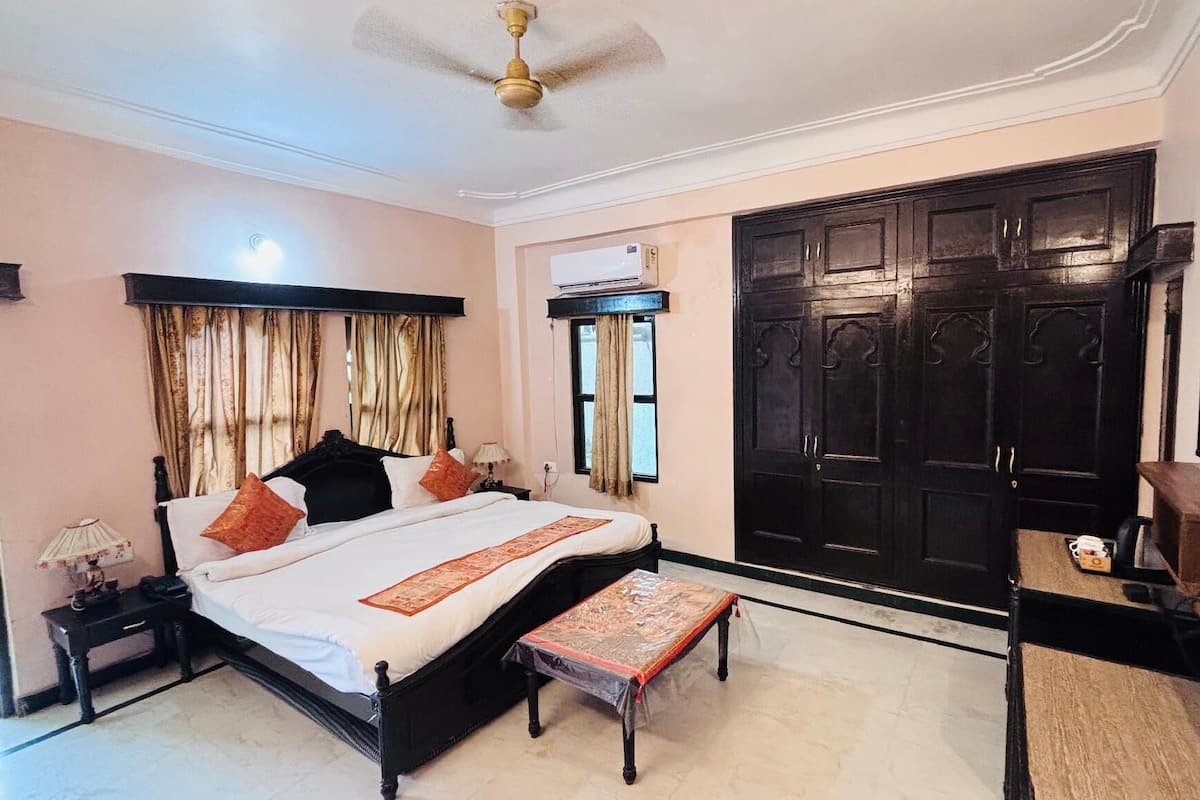 A bedroom with a bed, bedside table, lamp, window with curtains, wardrobe, and a television.
