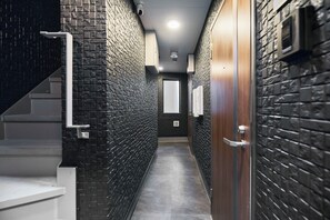 Un couloir étroit, avec un escalier sur la gauche, une porte en bois sur la droite et un mur dont le motif est constitué de briques.
