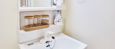 A white bathroom with a sink, mirror, and storage shelves.