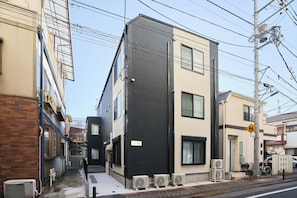 A multi-story building with external air conditioning units, a pedestrian crossing sign, and a bicycle parked outside. - Reberty Haneda (Ota-ku)
