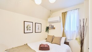 A neatly made bed with a folded towel, a bedside plant, and a wall-mounted air conditioner.