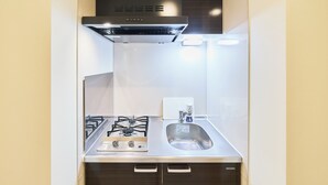 A compact kitchen with a gas stove, stainless steel sink, and a black range hood.