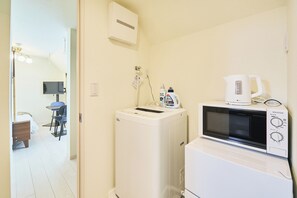 Une chambre d’hôtel compacte équipée d’un lave-linge, d’un four à micro-ondes, d’une petite table et d’une chaise.